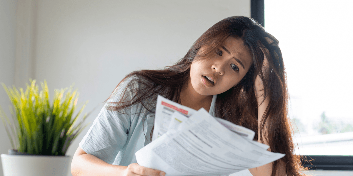 Ung person som ser överraskad och stressad ut över räkningar.