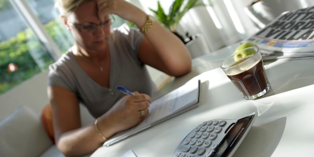 Kvinna använder miniräknare och betalar räkningar vid köksbordet, går igenom sin privatekonomi inför beslut om privatlån.