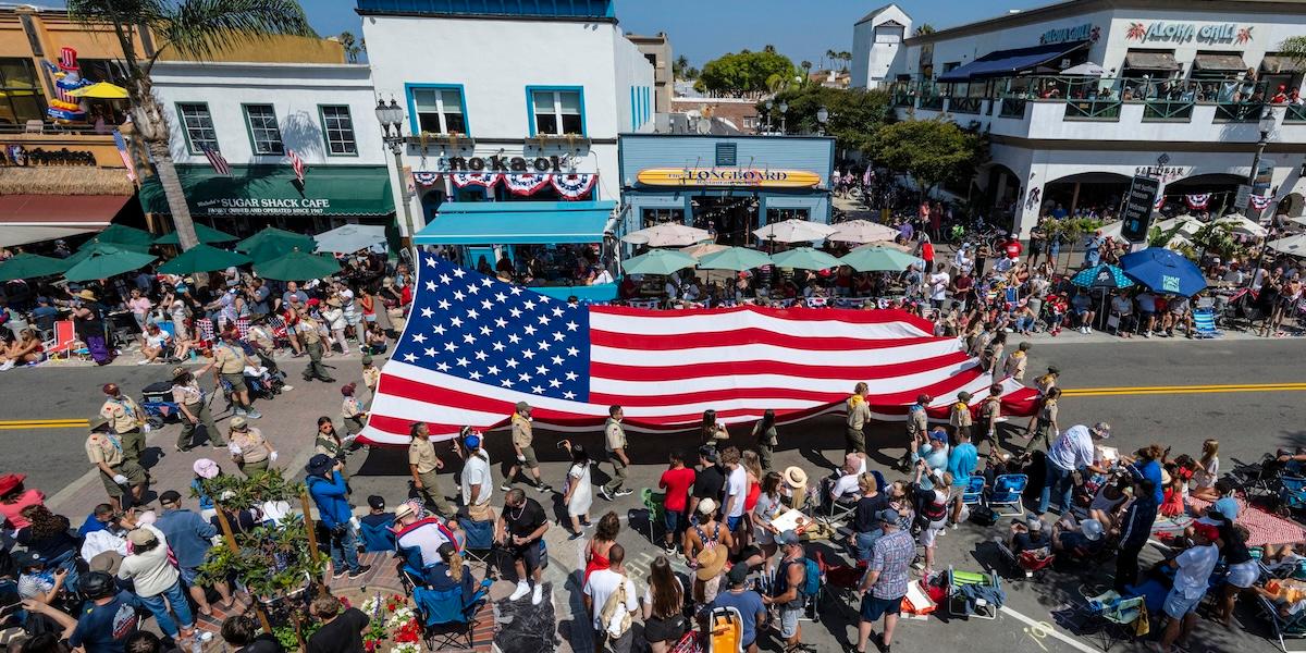 Stor amerikansk flagga bärs i parad på gata med folkmassa under en nationaldagsfirande i USA.