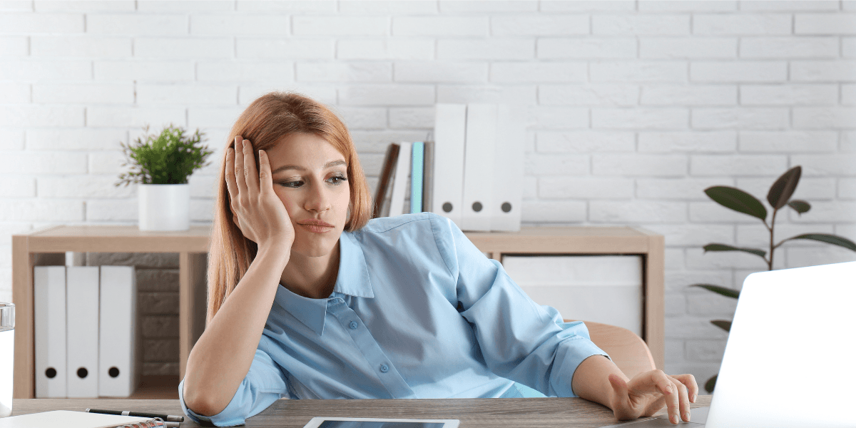 En ung kvinna stirrar uttråkat på sin datorskärm på ett kontor – signalerar låg motivation.