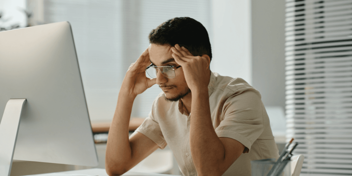 Stressad medarbetare framför dator i modern kontorsmiljö.