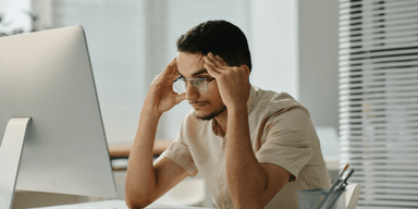 Stressad medarbetare framför dator i modern kontorsmiljö.