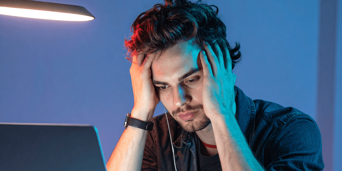 Ung man sitter framför laptop med händerna mot huvudet, ser frustrerad ut – symboliserar osäkerhet kring karriär och framtid.