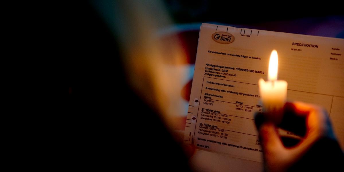 En person håller ett stearinljus i mörker medan de läser sin elräkning från DinEl – symboliserar oro för höga elpriser vintertid.